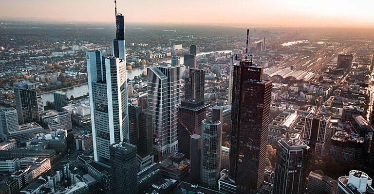 Luftaufnahme der Frankfurter Bankenskyline mit ihren Hochhäusern und dem Main bei Sonnenuntergang.