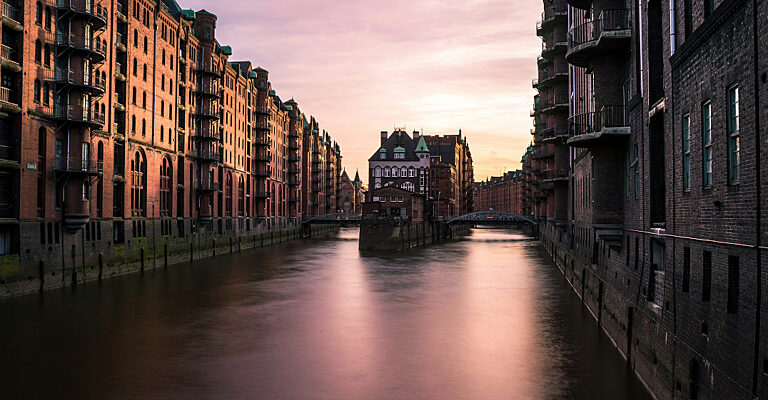 Die Hamburger Speicherstadt mit dem Wasserschloss und den Backsteinbauten entlang des Kanals in der Abenddämmerung.